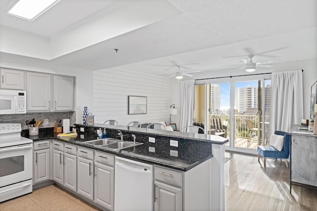 kitchen featuring sink, backsplash, kitchen peninsula, dark stone counters, and white appliances