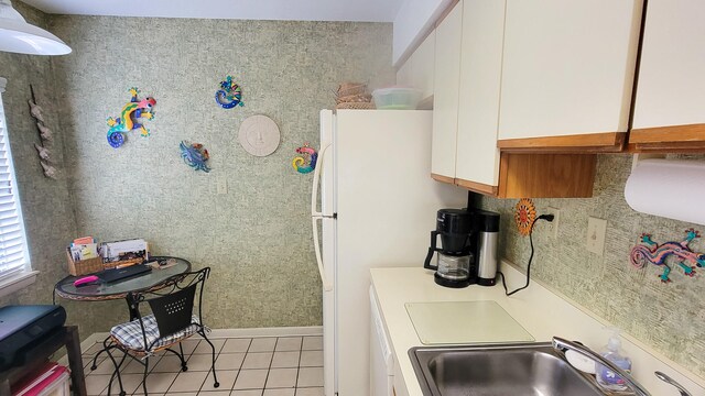 kitchen with white cabinets, sink, light tile flooring, and white fridge