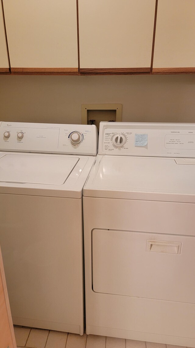 laundry room featuring cabinets, hookup for a washing machine, light tile flooring, and washing machine and clothes dryer