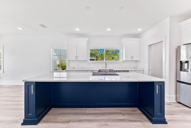 kitchen featuring light wood-type flooring, white cabinetry, stainless steel fridge, and light stone counters