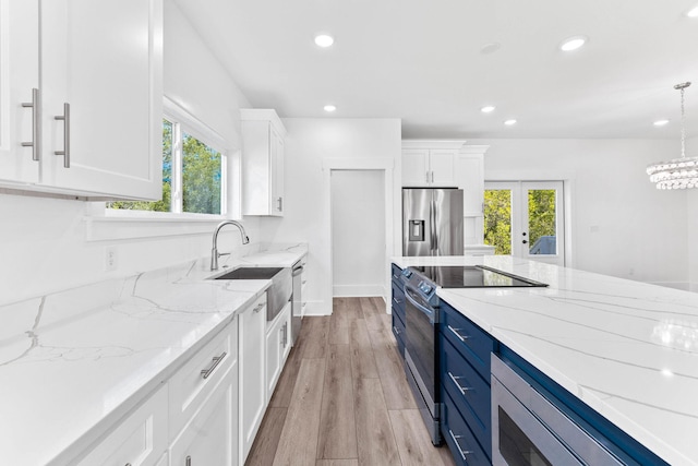 kitchen featuring pendant lighting, white cabinets, appliances with stainless steel finishes, blue cabinetry, and light stone counters