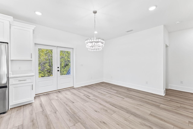 unfurnished dining area with french doors, light hardwood / wood-style flooring, and a chandelier