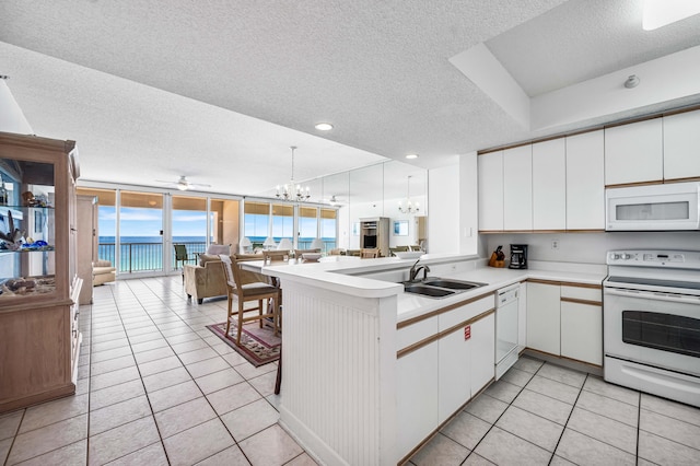 kitchen featuring a wall of windows, sink, kitchen peninsula, light tile patterned flooring, and white appliances