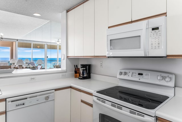 kitchen featuring a textured ceiling, white appliances, and white cabinetry