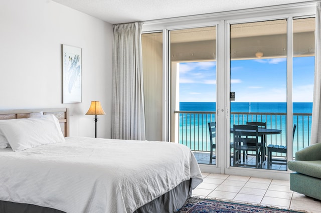 bedroom featuring a textured ceiling, access to exterior, a water view, and light tile patterned floors