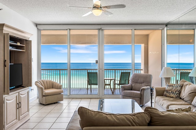 living room with a textured ceiling, ceiling fan, a water view, and light tile patterned floors