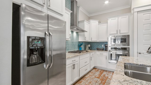 kitchen featuring backsplash, stainless steel appliances, wall chimney range hood, white cabinetry, and light wood-type flooring