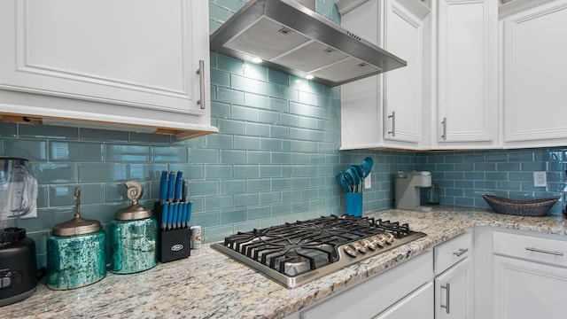 kitchen featuring backsplash, wall chimney range hood, stainless steel gas stovetop, and white cabinets