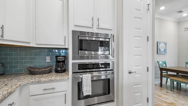 kitchen with light stone counters, white cabinetry, stainless steel appliances, ornamental molding, and light hardwood / wood-style flooring