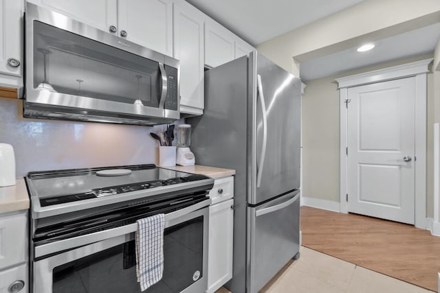 kitchen with appliances with stainless steel finishes, white cabinetry, and light tile flooring