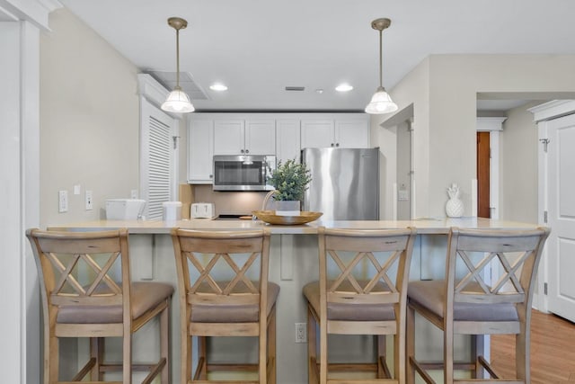 kitchen with appliances with stainless steel finishes, a kitchen bar, hanging light fixtures, light hardwood / wood-style flooring, and kitchen peninsula