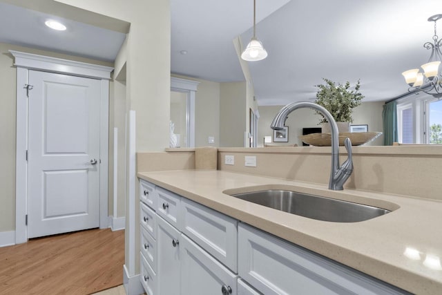 kitchen with hanging light fixtures, white cabinetry, sink, light wood-type flooring, and a chandelier