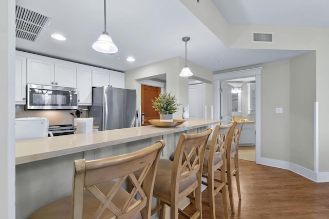 kitchen featuring a kitchen breakfast bar, white cabinets, light wood-type flooring, kitchen peninsula, and appliances with stainless steel finishes