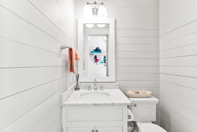 bathroom featuring wood walls, vanity, and toilet