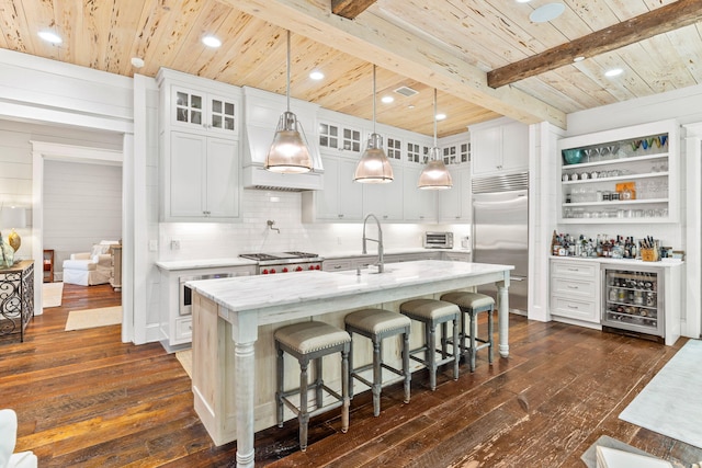 kitchen with wine cooler, a kitchen island with sink, dark hardwood / wood-style flooring, appliances with stainless steel finishes, and tasteful backsplash