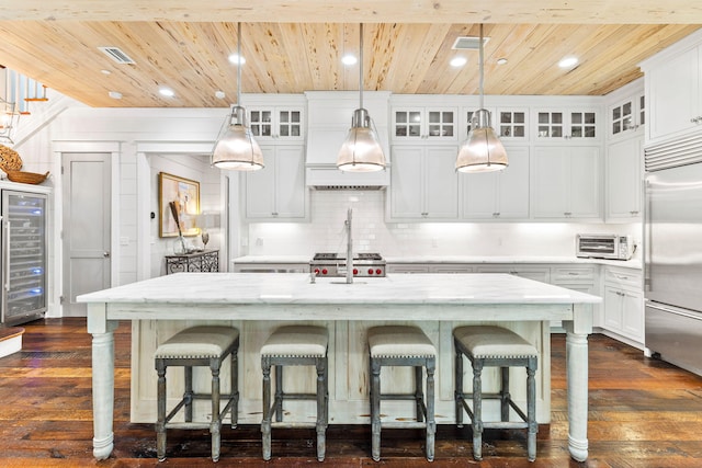 kitchen featuring tasteful backsplash, built in refrigerator, dark hardwood / wood-style floors, a center island with sink, and pendant lighting