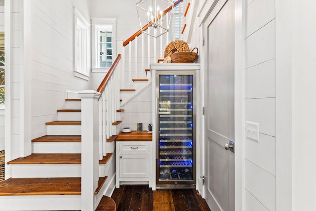 stairs with dark hardwood / wood-style floors, an inviting chandelier, and beverage cooler