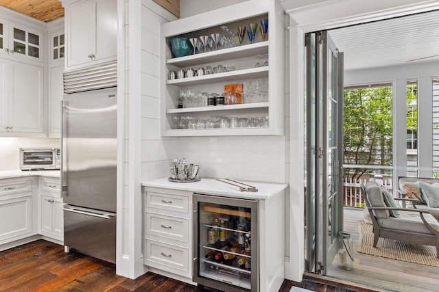 bar with dark wood-type flooring, stainless steel built in fridge, white cabinetry, and beverage cooler