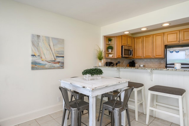 kitchen with a kitchen breakfast bar, light stone countertops, backsplash, and appliances with stainless steel finishes