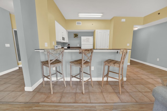 kitchen featuring white appliances, a kitchen bar, kitchen peninsula, and white cabinetry