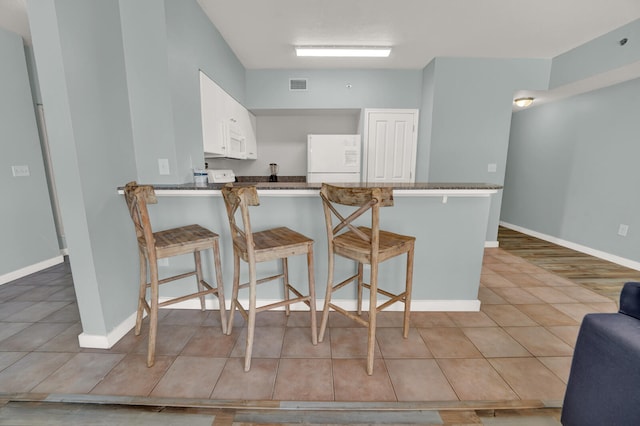 kitchen featuring kitchen peninsula, a breakfast bar, white fridge, and white cabinetry