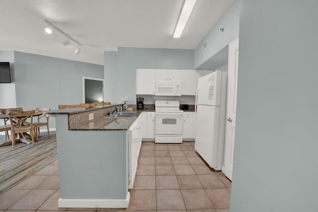 kitchen with light tile floors, white cabinets, white appliances, kitchen peninsula, and dark stone countertops