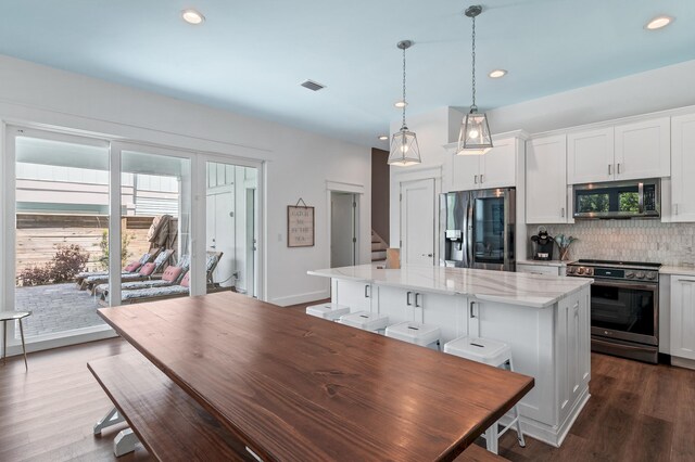 kitchen with backsplash, wood-type flooring, stainless steel appliances, and hanging light fixtures