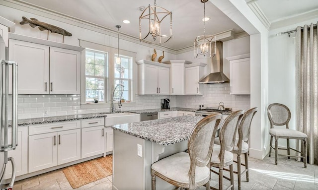 kitchen featuring a breakfast bar, sink, wall chimney range hood, white cabinets, and a center island