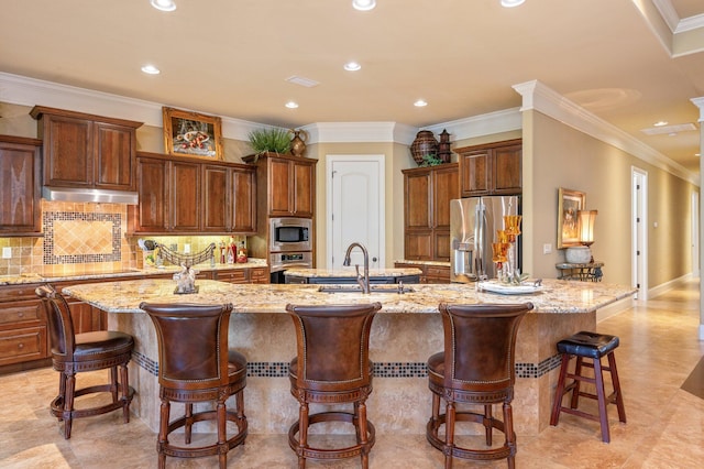 kitchen featuring appliances with stainless steel finishes, light tile flooring, light stone counters, sink, and a large island with sink