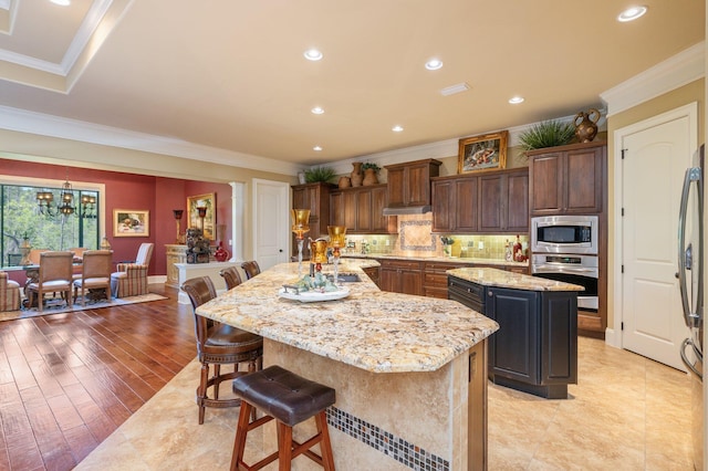 kitchen with light stone counters, appliances with stainless steel finishes, a center island, light hardwood / wood-style flooring, and a kitchen breakfast bar