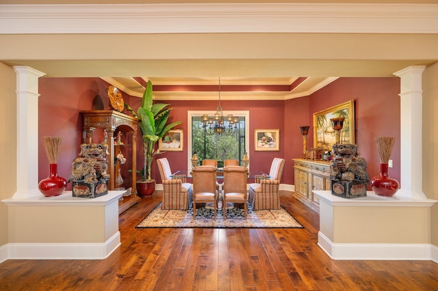 dining room with hardwood / wood-style floors, a notable chandelier, crown molding, and decorative columns