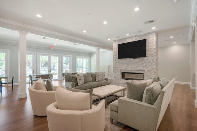 living room with ornamental molding, a stone fireplace, dark wood-type flooring, and decorative columns