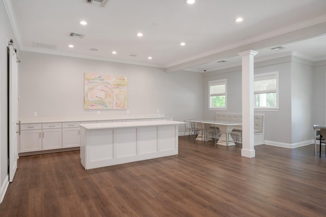 kitchen with a kitchen island, decorative columns, dark wood-type flooring, white cabinets, and ornamental molding