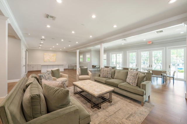 living room with crown molding, decorative columns, and light wood-type flooring