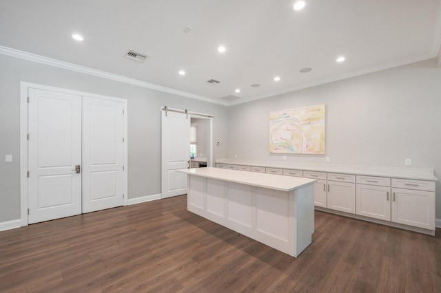 kitchen with white cabinetry, dark hardwood / wood-style floors, ornamental molding, a barn door, and a kitchen island