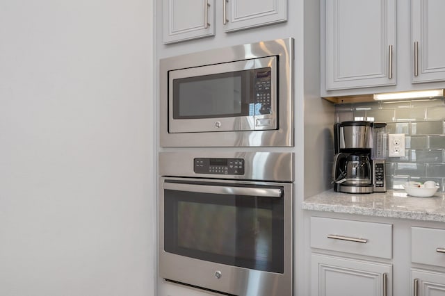 kitchen featuring tasteful backsplash, white cabinetry, stainless steel appliances, and light stone countertops