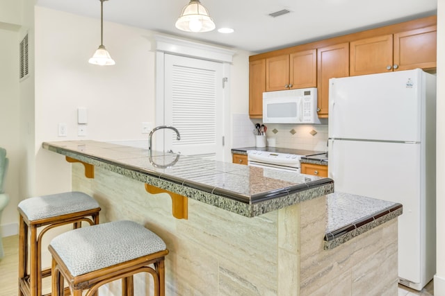 kitchen with kitchen peninsula, decorative backsplash, white appliances, hanging light fixtures, and a breakfast bar area