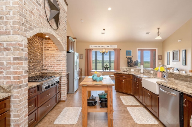 kitchen with light stone countertops, sink, stainless steel appliances, pendant lighting, and an inviting chandelier