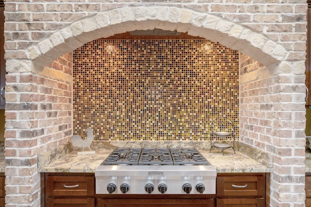 kitchen featuring stainless steel gas cooktop, brick wall, decorative backsplash, and light stone counters