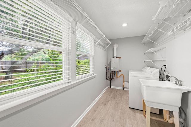 laundry room featuring light hardwood / wood-style floors, sink, tankless water heater, and washing machine and clothes dryer