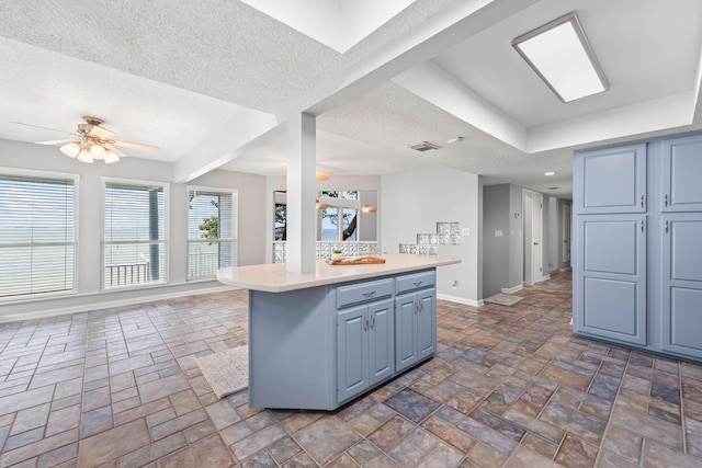 kitchen with a kitchen breakfast bar, a textured ceiling, ceiling fan, blue cabinetry, and a center island