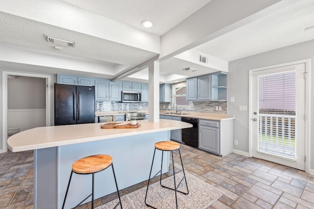 kitchen featuring sink, a textured ceiling, a kitchen bar, decorative backsplash, and black appliances