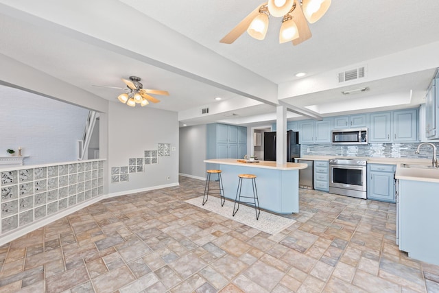 kitchen featuring a kitchen breakfast bar, sink, decorative backsplash, blue cabinetry, and appliances with stainless steel finishes