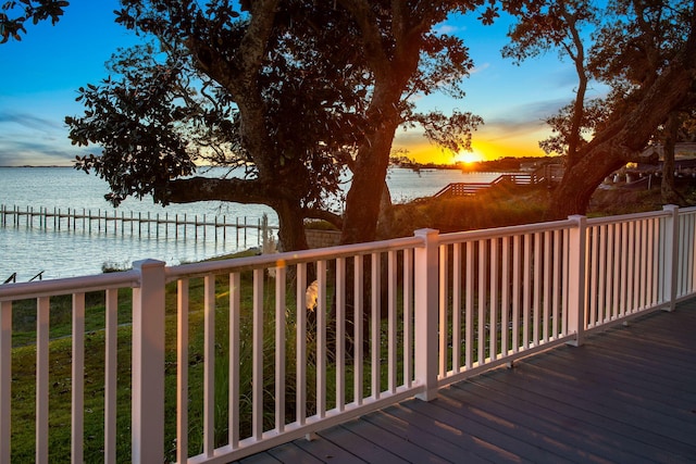 deck at dusk with a water view and a dock