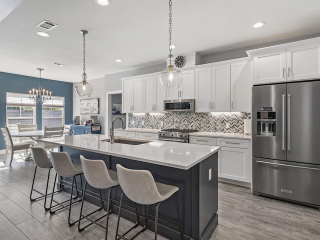 kitchen featuring high end appliances, white cabinetry, backsplash, sink, and an island with sink