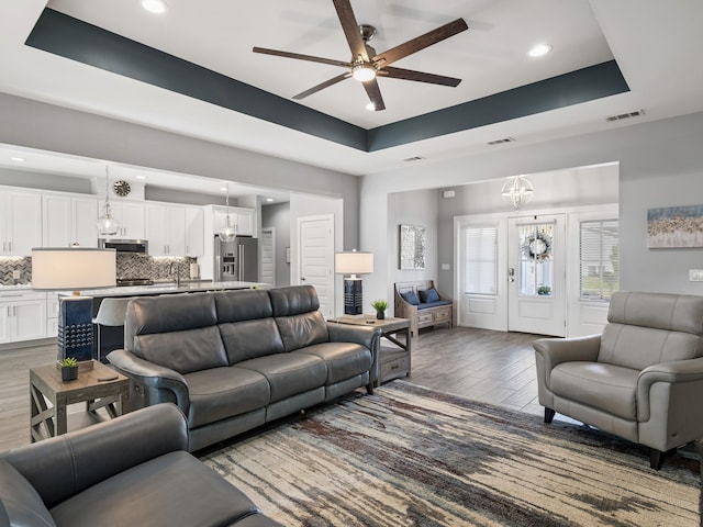 living room featuring hardwood / wood-style floors, ceiling fan with notable chandelier, and a raised ceiling