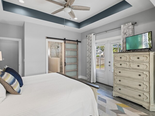 bedroom with wood-type flooring, ceiling fan, a barn door, and a tray ceiling