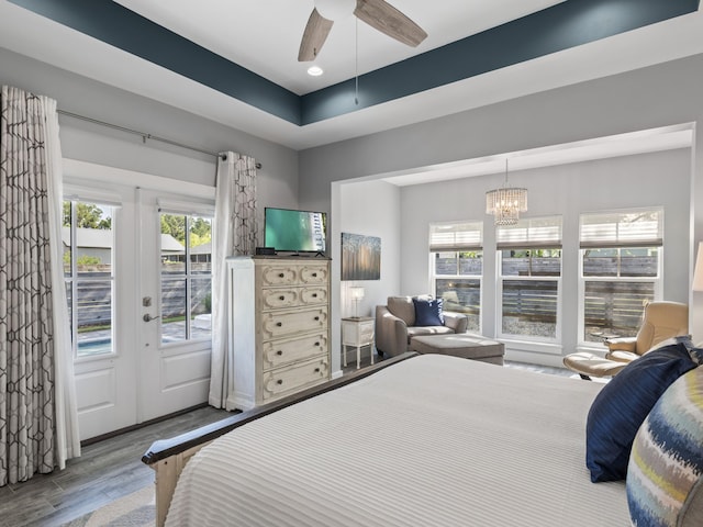 bedroom with ceiling fan with notable chandelier, french doors, access to outside, and hardwood / wood-style floors