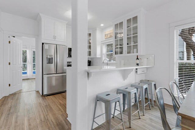 kitchen featuring white cabinetry, sink, stainless steel fridge, light hardwood / wood-style floors, and a breakfast bar