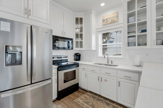 kitchen with light stone countertops, sink, stainless steel appliances, wood-type flooring, and white cabinets